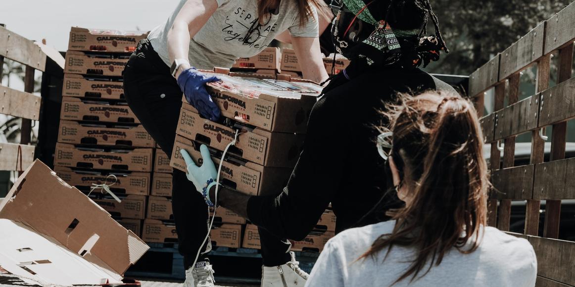A volunteer is standing on the back of a truck, passing boxes of strawberries to other people.