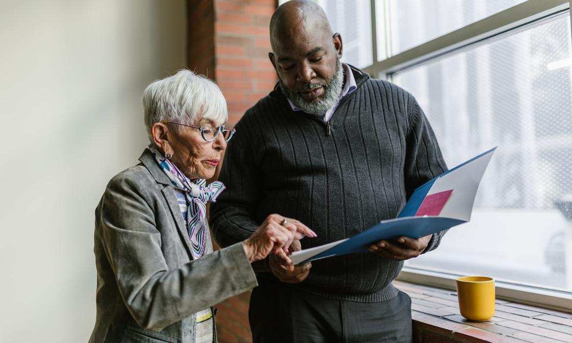 Two people are standing next to each other, looking at an open folder.