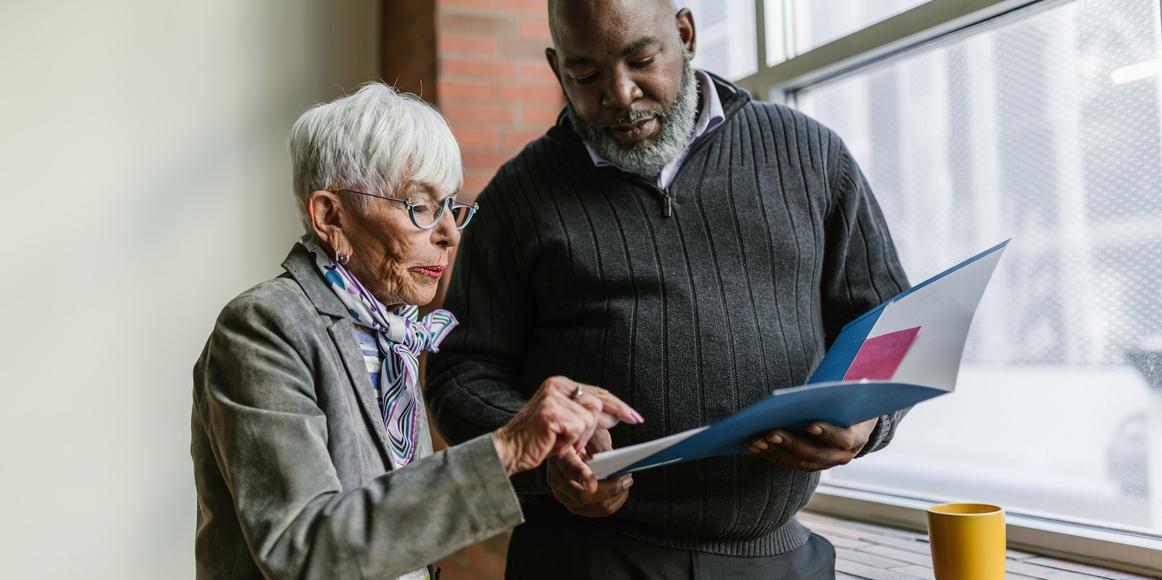 Two people are standing next to each other, looking at an open folder.