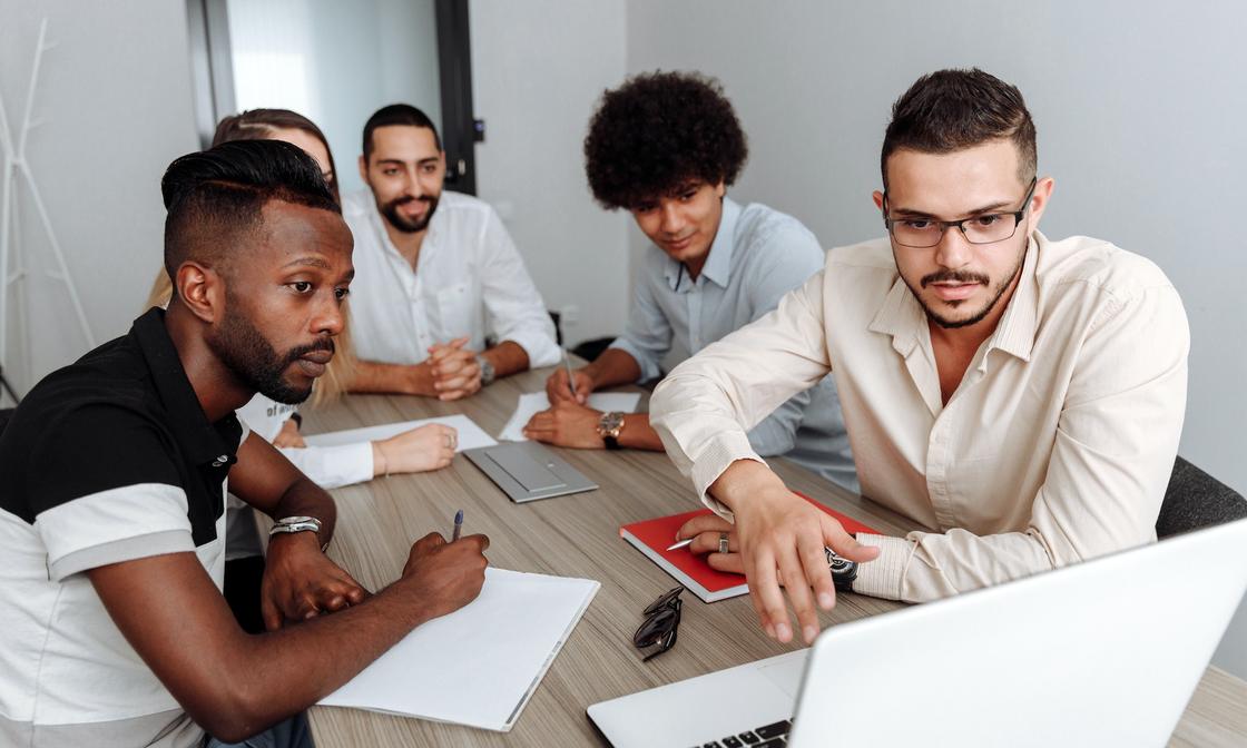 A group of colleagues all sitting around a desk, each looking intently at a laptop.