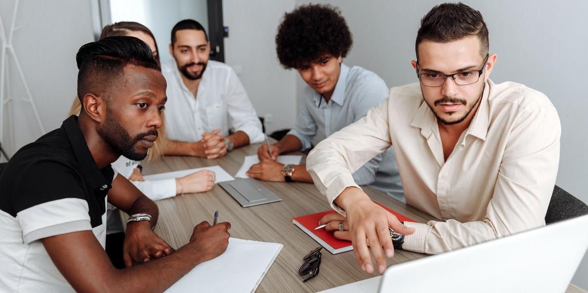 A group of colleagues all sitting around a desk, each looking intently at a laptop.