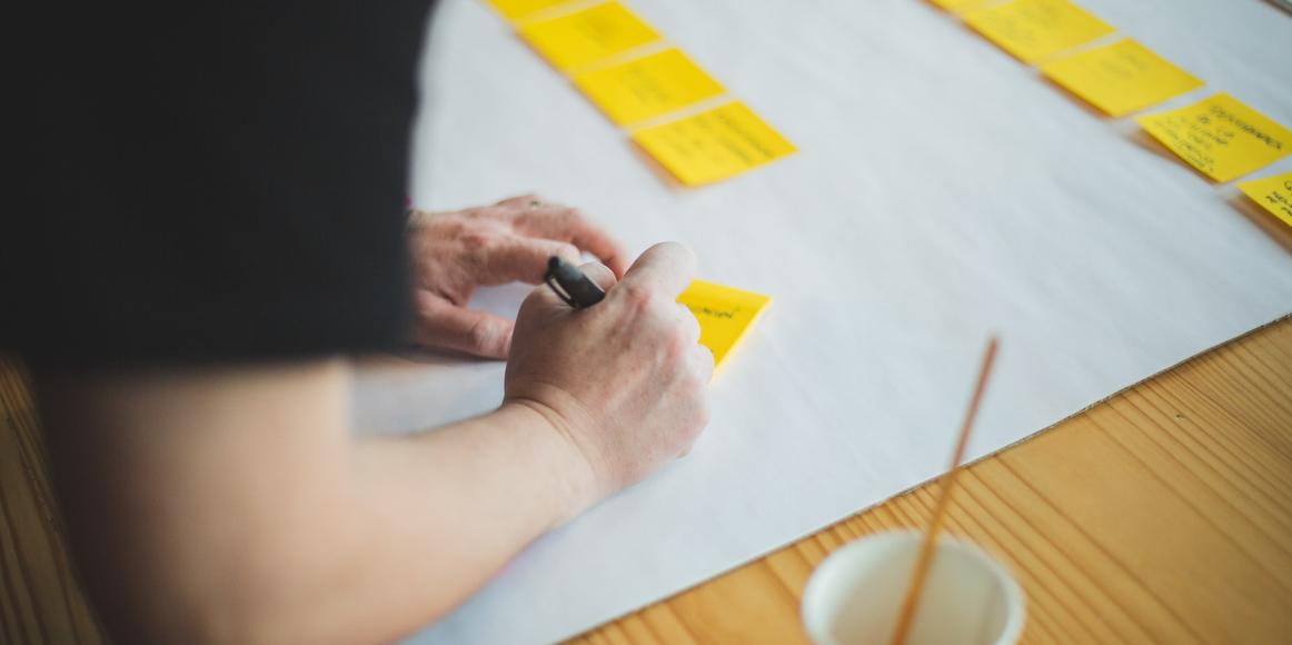 Someone is writing on yellow post-it notes and sticking them on a large piece of paper in 2 horizontal lines.