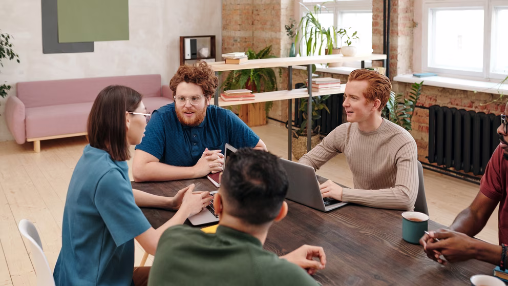 A group of millennial-aged colleagues sitting around a table min-discussion.