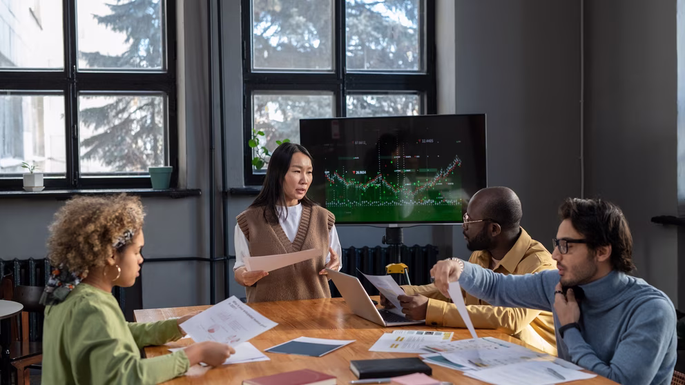 A group of accountants huddled around a desk, poring over paper charts.