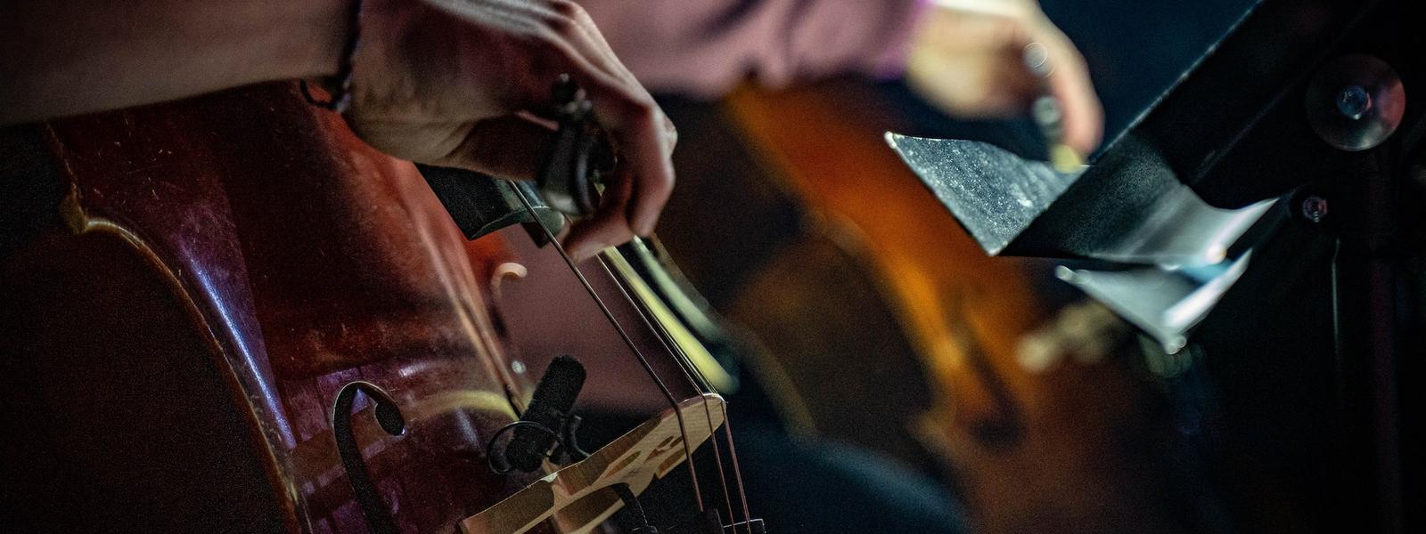 Two people play the cello reading from sheet music.