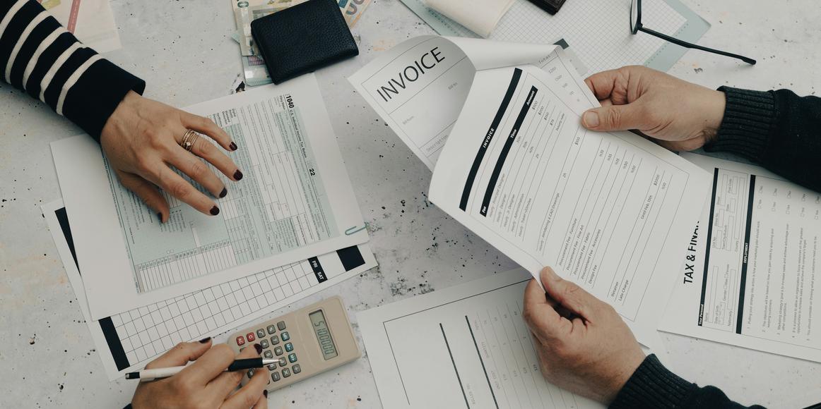 Two people working on invoices and tax forms, highlighting the importance of a systematic bookkeeping cleanup process.