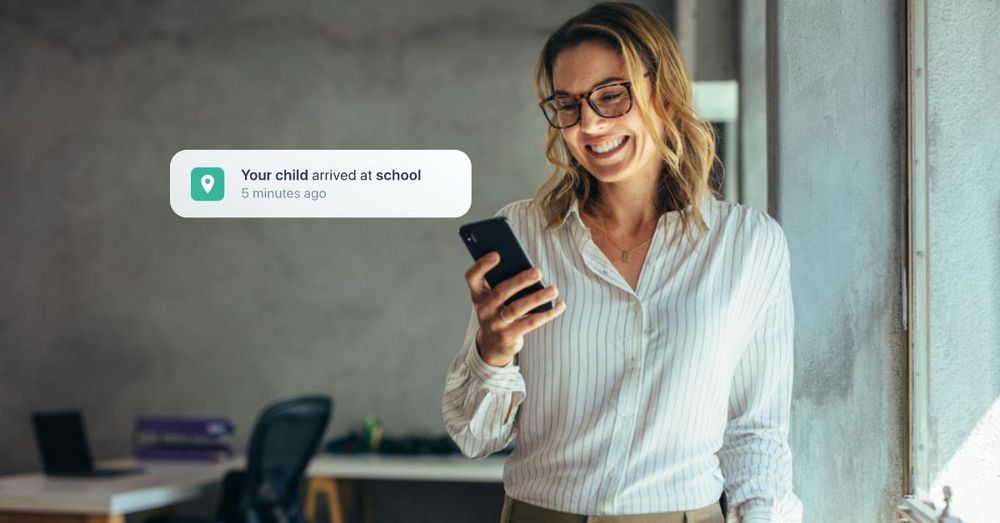 Business woman looks at her phone with a smile, she just got the notification that her child arrived safely at school