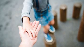 Child balancing on obstacles, reaching out to hold parent's hand