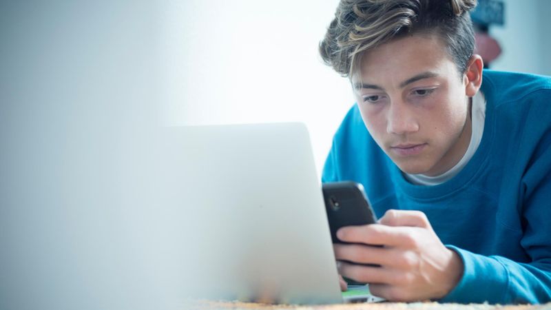 Teenage boy looking at his phone and laptop at the same time