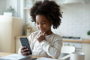 Little girl is doing her homework with the help of a smartphone