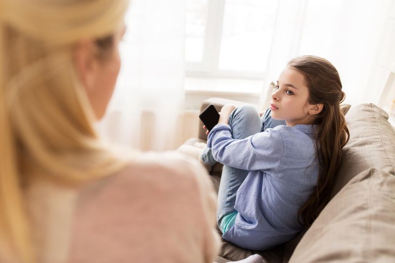 sad girl with smartphone looking at her mother at home