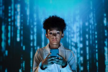 boy looking at camera, holding his cell phone, stands in front of blue matrix-like background