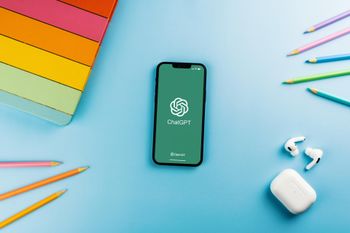 smartphone in the middle of the picture shows the chatgpt logo, phone is surrounded by school material like pens and a colorful folder
