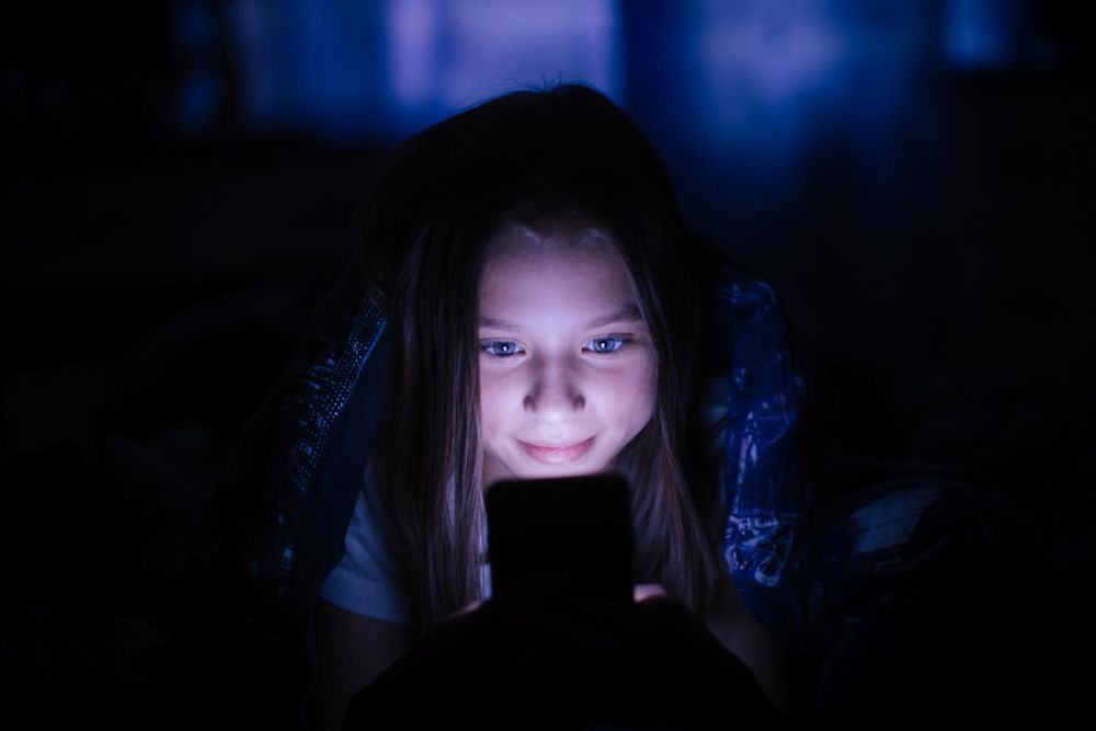 Little girl at night under a blanket looking at the smartphone