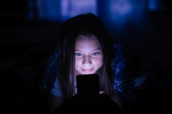 Little girl at night under a blanket looking at the smartphone