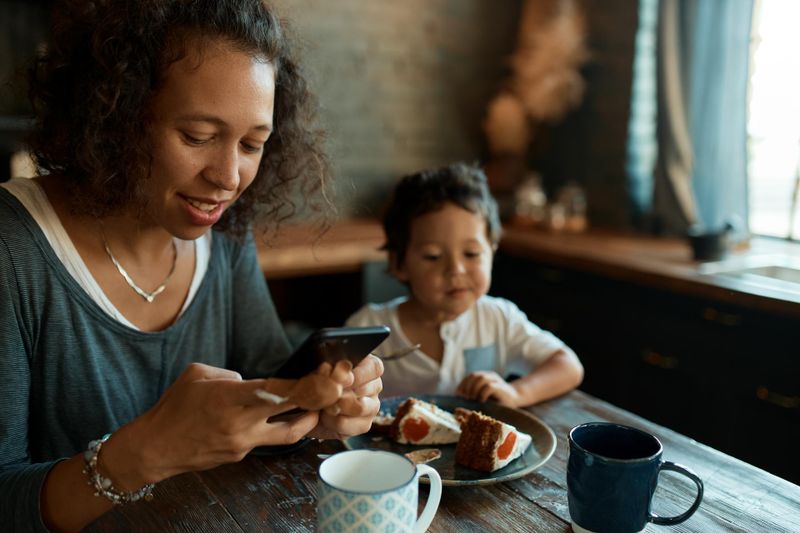 Young mother sits on the table with her young son and looks at her smartphone