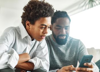 Teenage boy looking at father's phone, father holds the phone while smiling