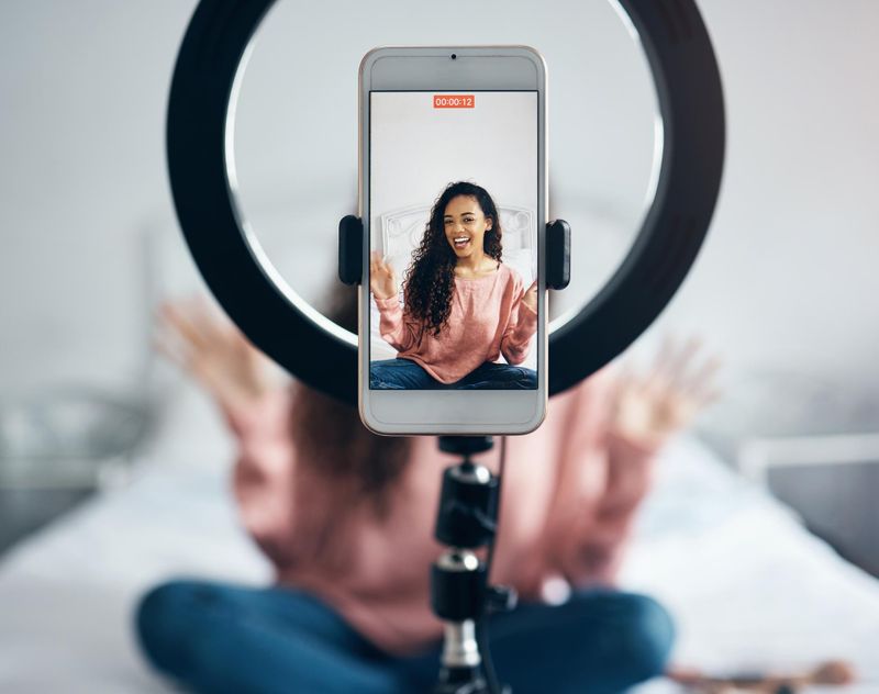 Teenager sits on her bed and is filming a video for social media on her phone