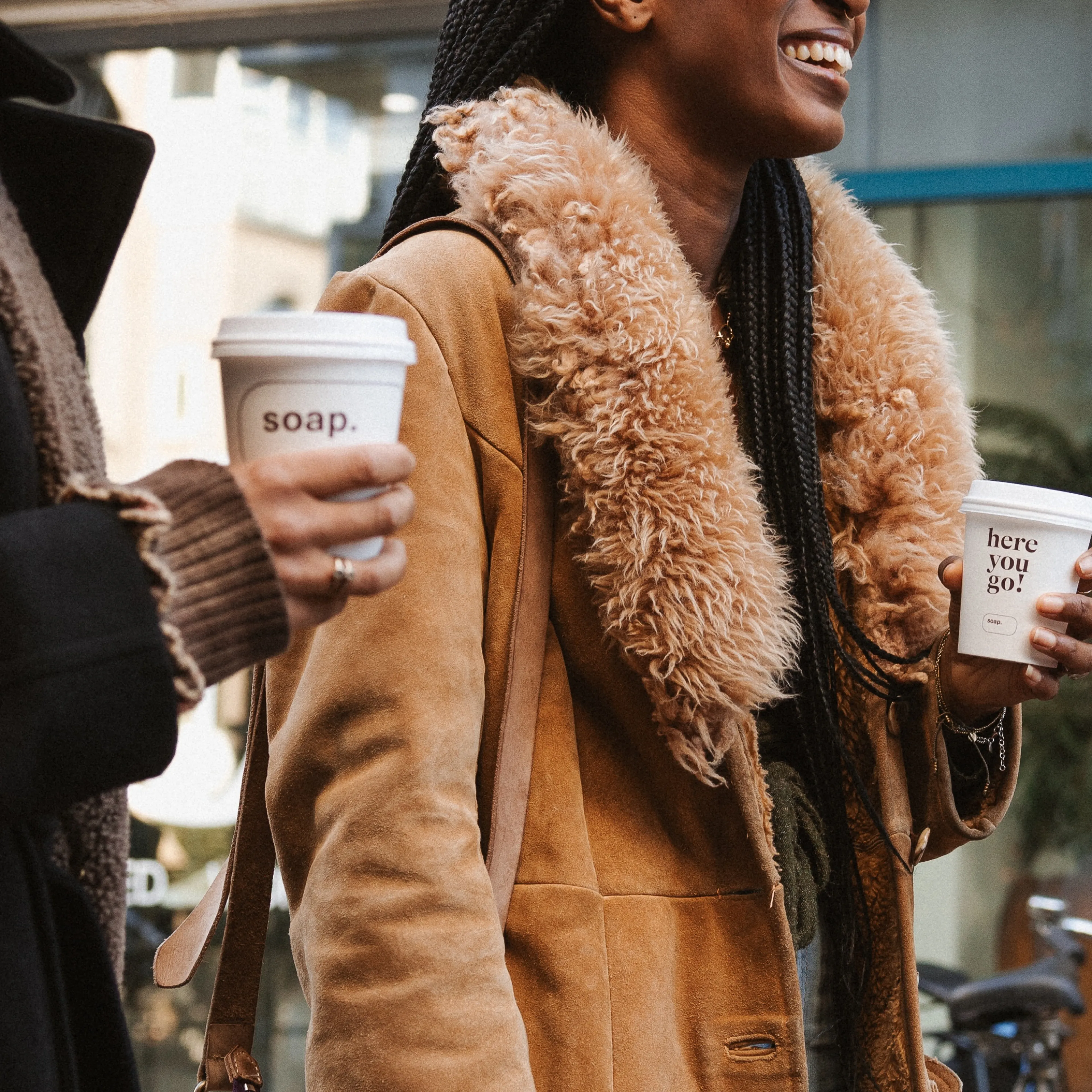 Een lachende vrouw loopt over straat met een to-go koffiebeker van Soap