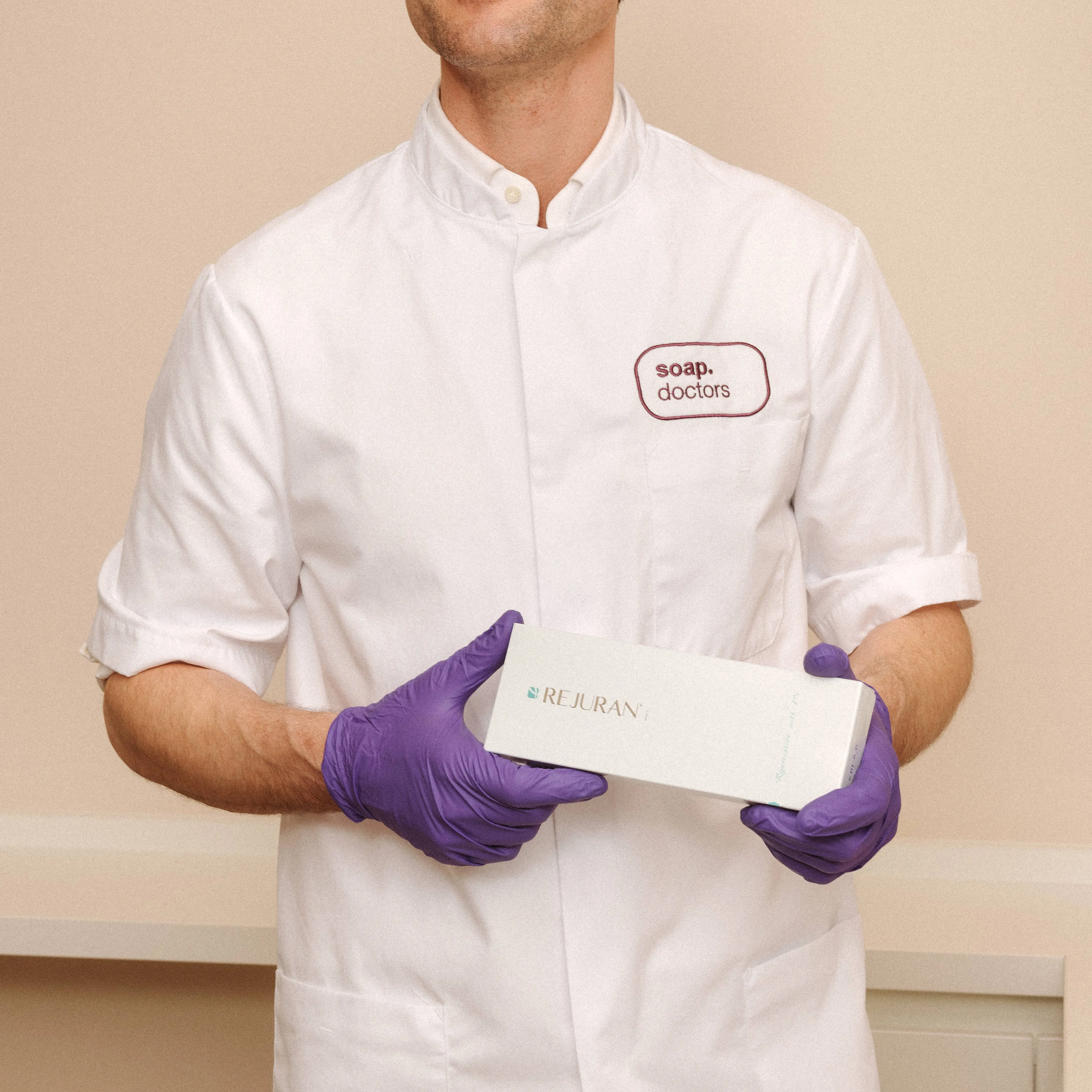 A person in a white coat and purple gloves holds a box labeled "Rejuran" with "soap. doctors" embroidered on the coat.