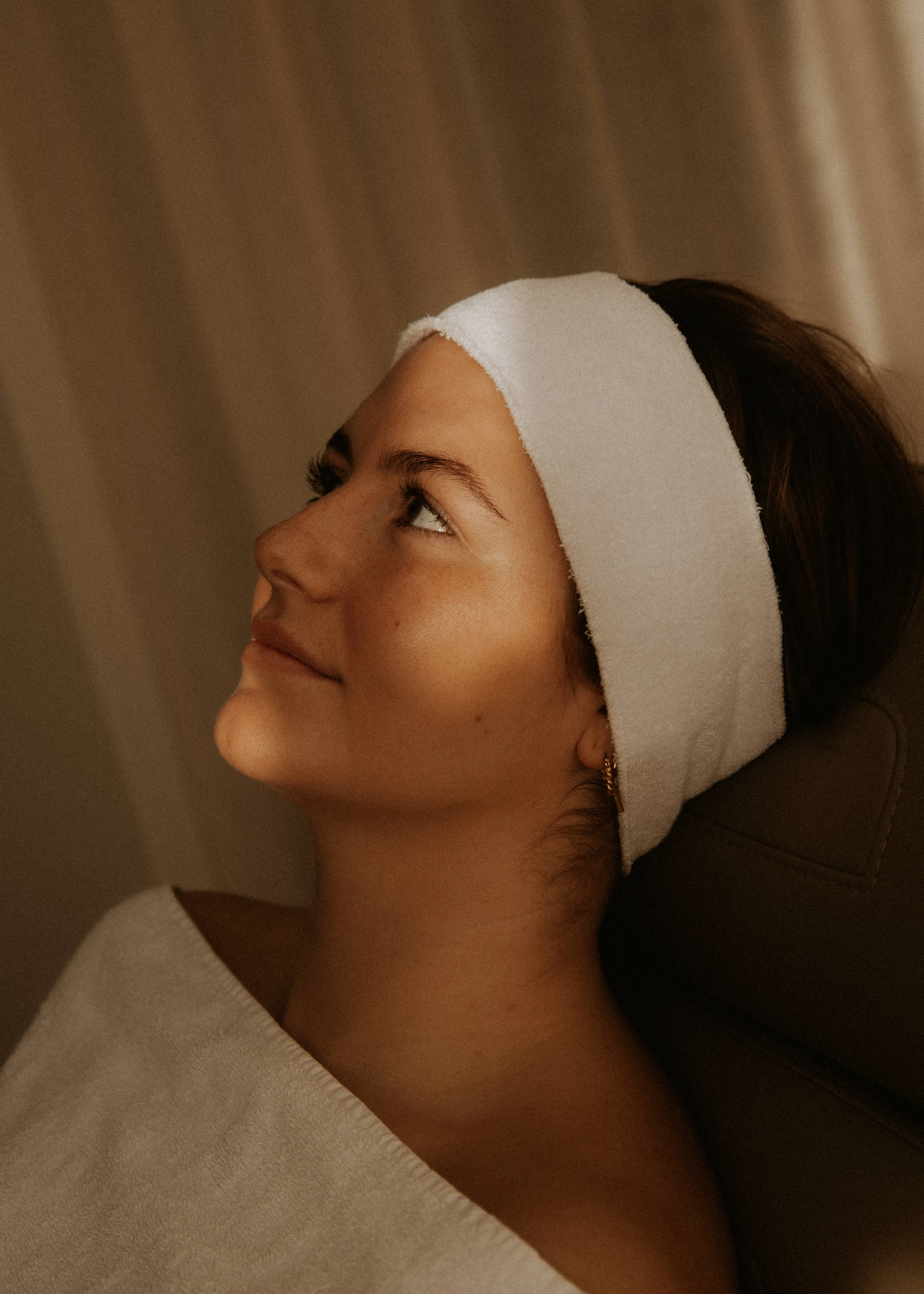 Vrouw met een hoofdband ontspant in de behandelstoel tijdens een facial