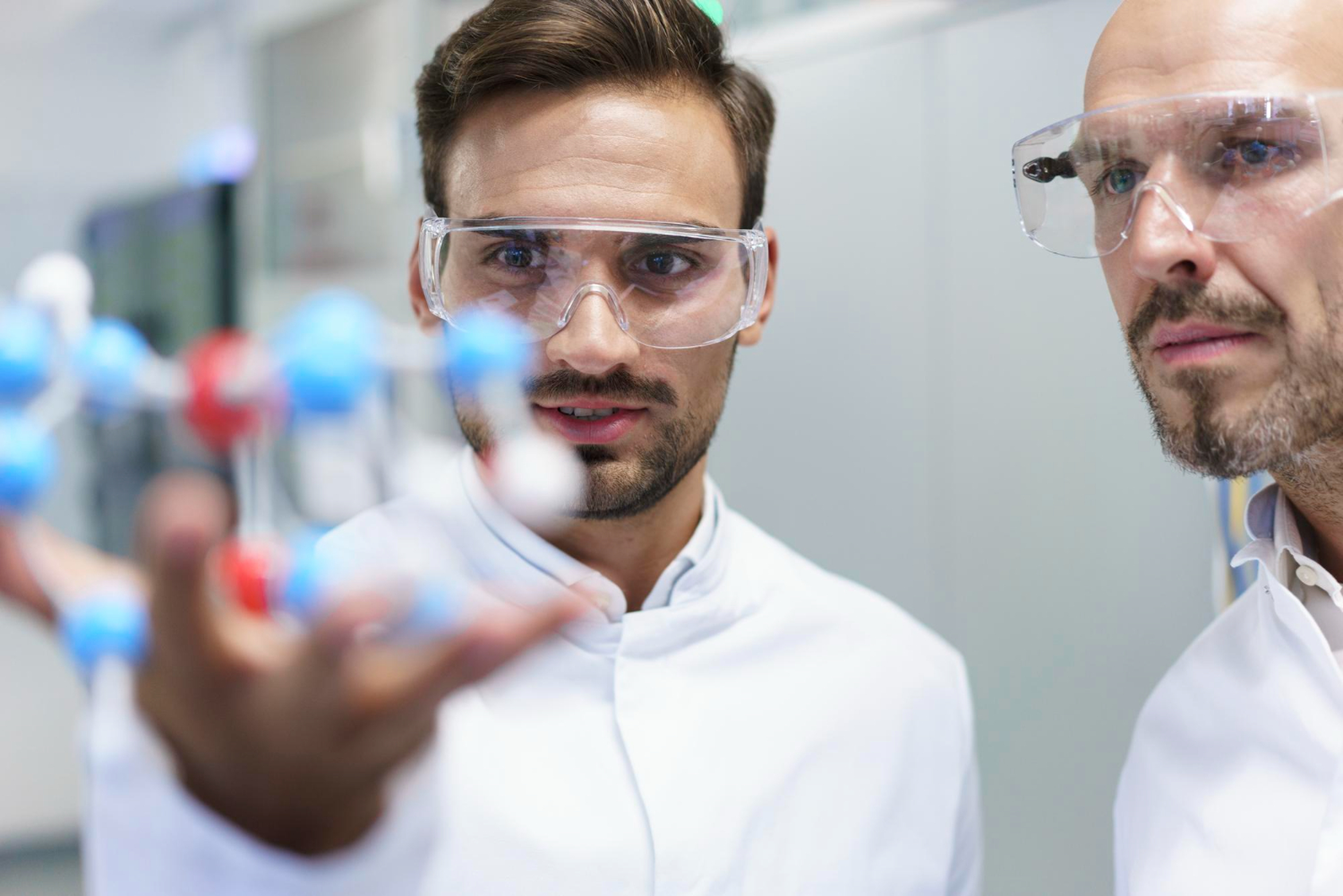 zwei Personen mit Schutzbrille betrachten ein Atommodell