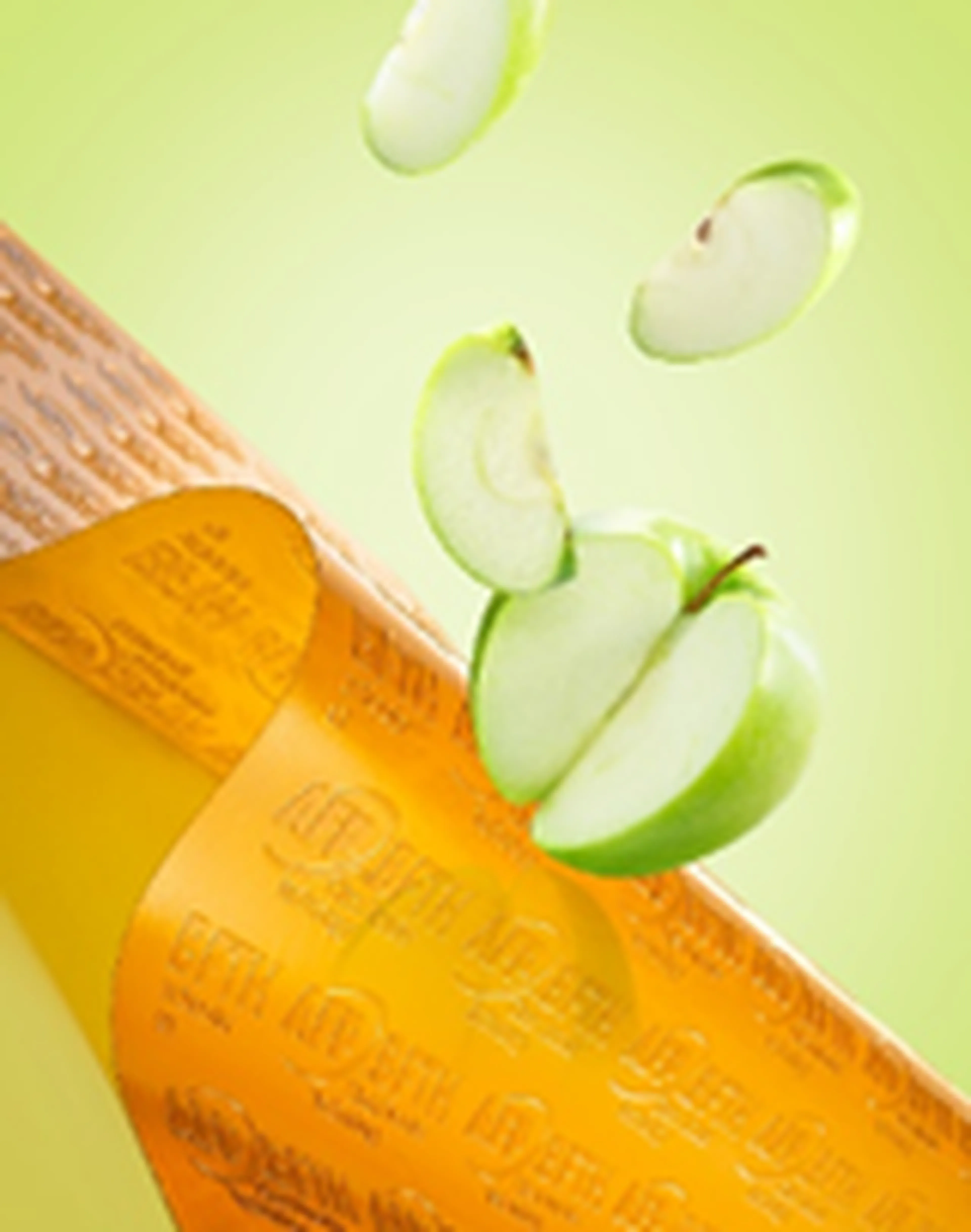 Sliced green apples with caramel sauce drizzled from a wooden spoon on a gradient green background.