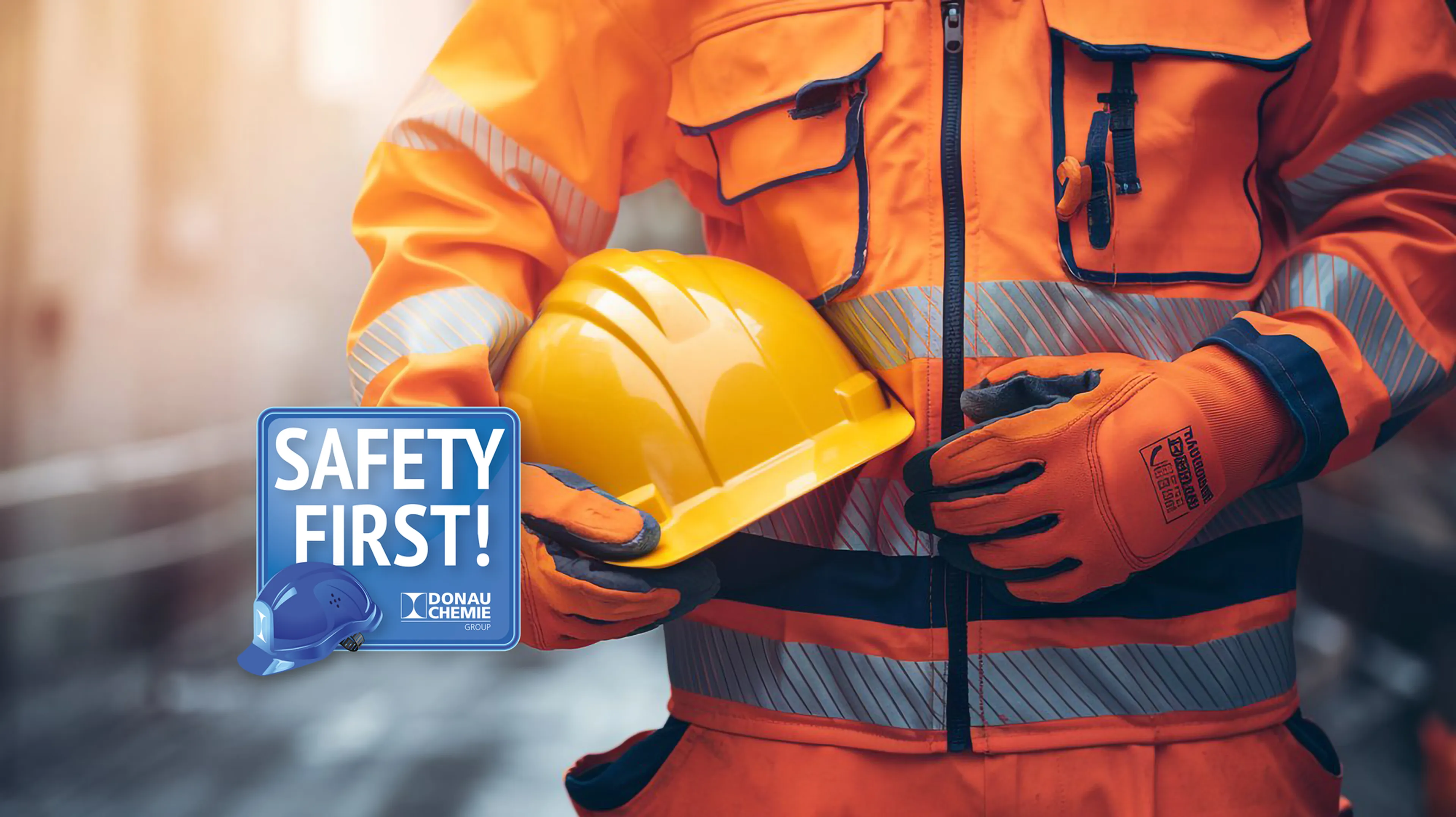 Construction worker in orange safety gear holding a yellow hard hat. A "Safety First" sign with blue helmet is visible.