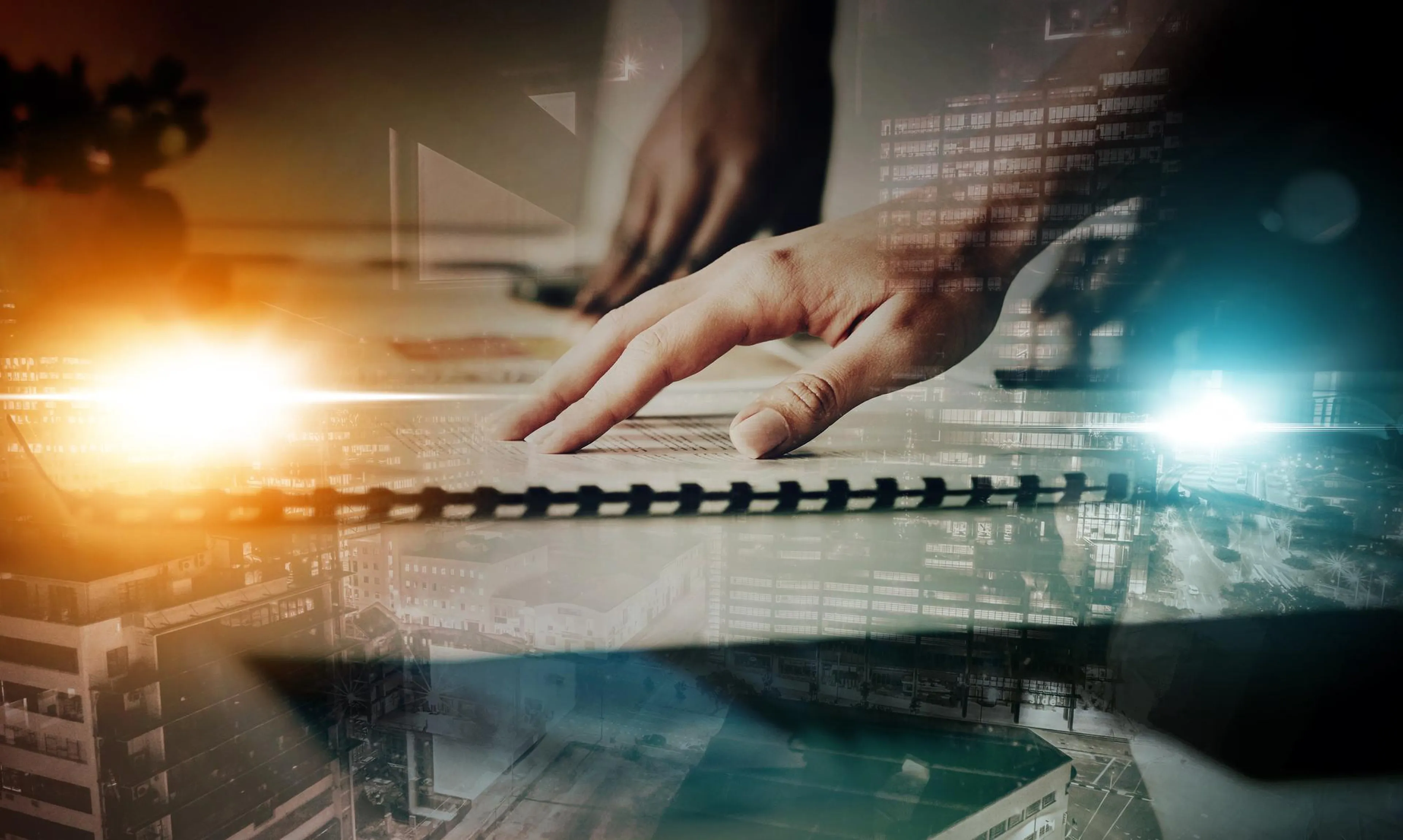 A hand touches a spiral-bound notebook with a futuristic cityscape overlay, illuminated by warm and cool lights.