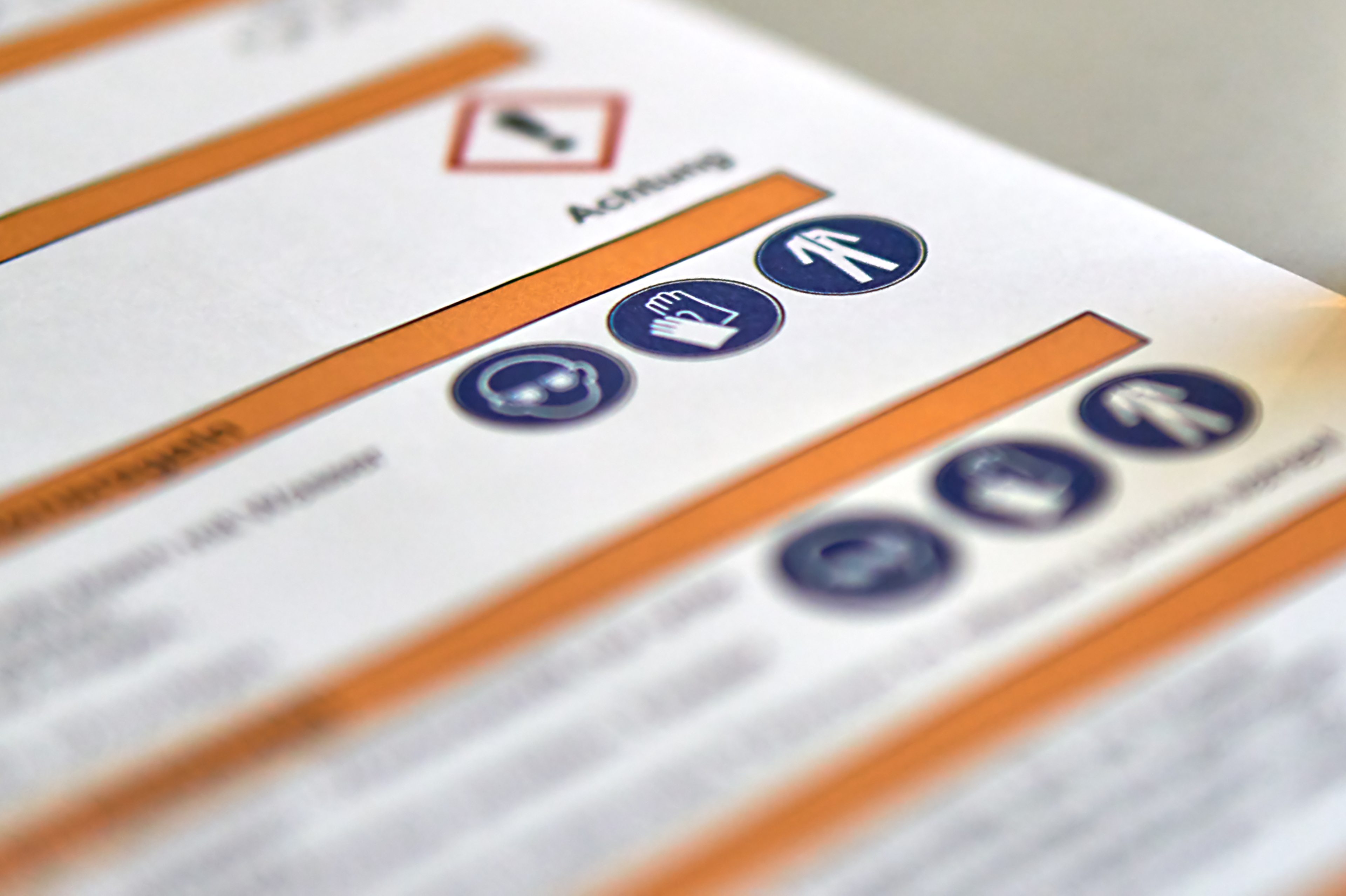 Close-up of a safety manual, featuring warning icons and symbols, including a hand, a helmet, and a person, with blurred text in the background.