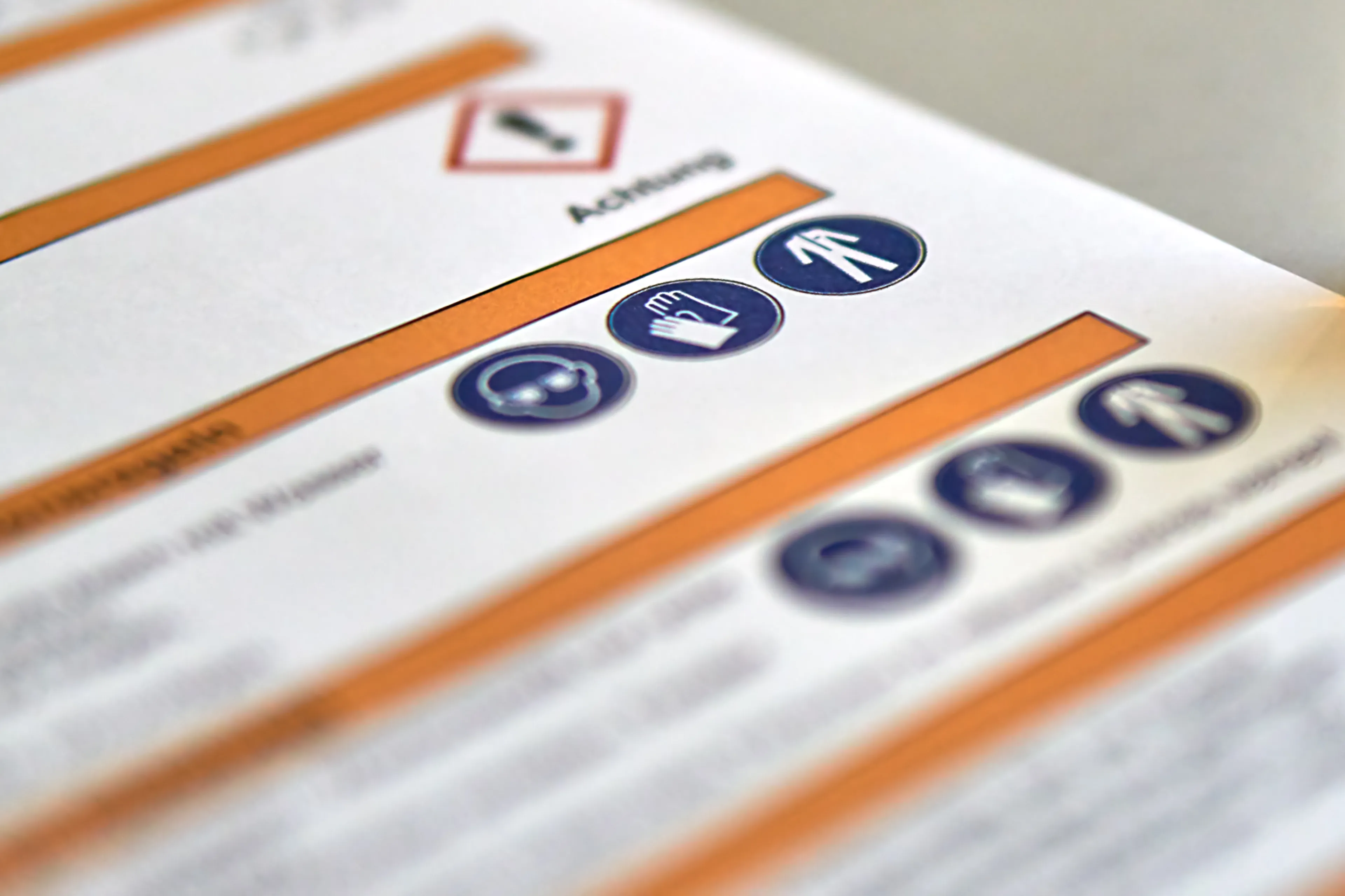 Close-up of a safety manual, featuring warning icons and symbols, including a hand, a helmet, and a person, with blurred text in the background.