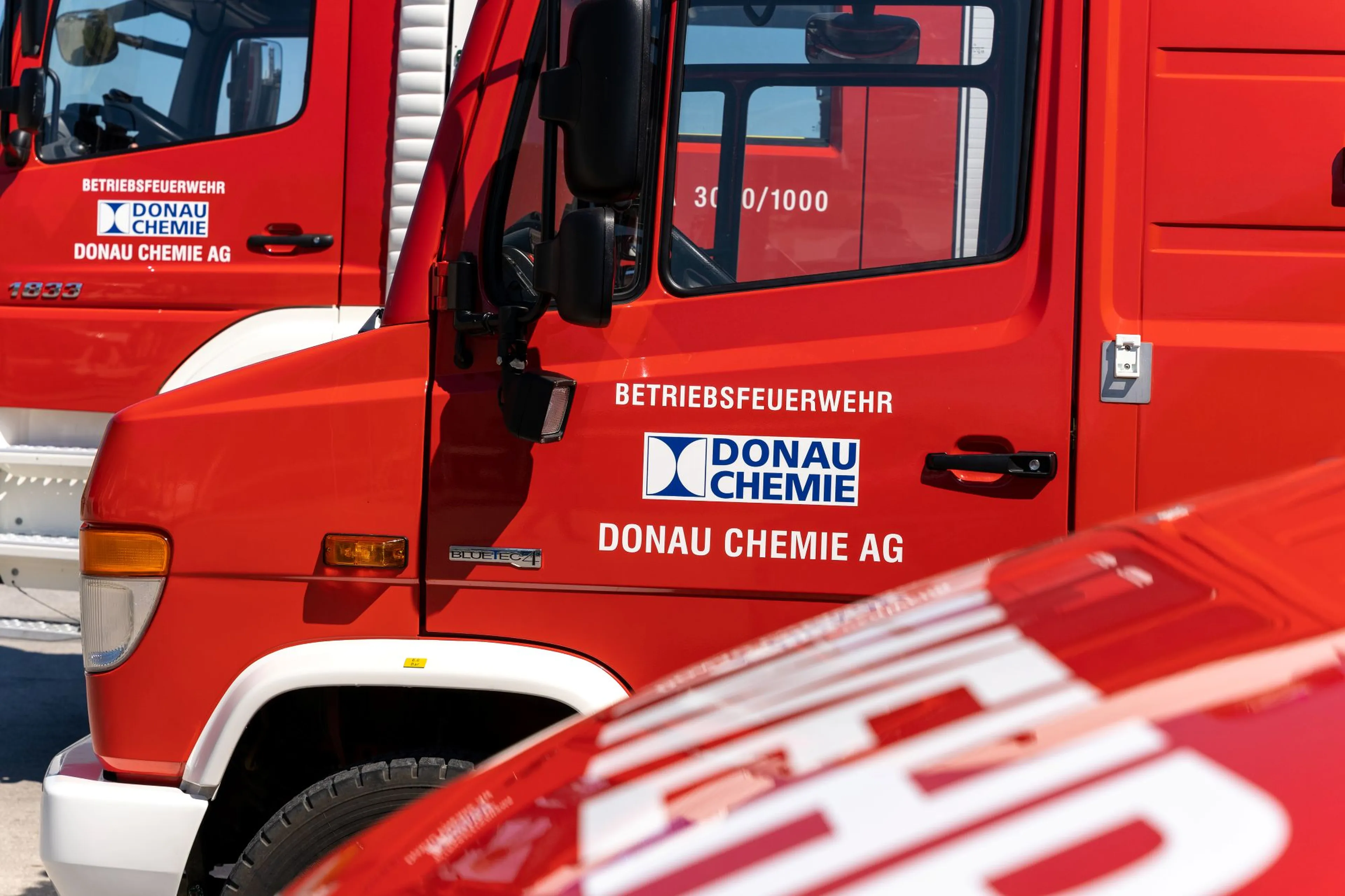 Red fire trucks with "Betriebsfeuerwehr Donau Chemie AG" logos, parked outdoors on a sunny day.
