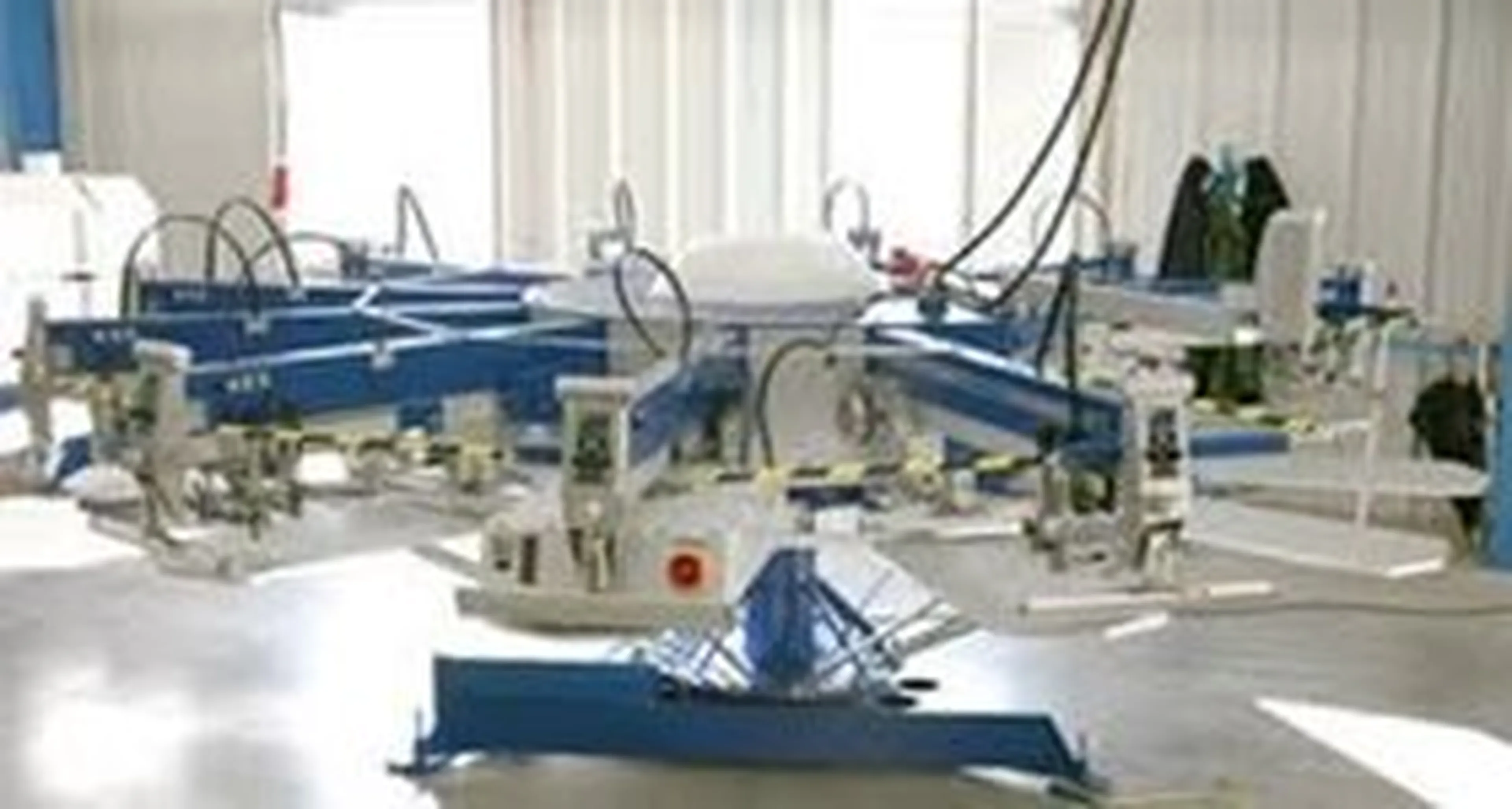 A large industrial screen printing machine with multiple arms and clamps in a well-lit workspace.