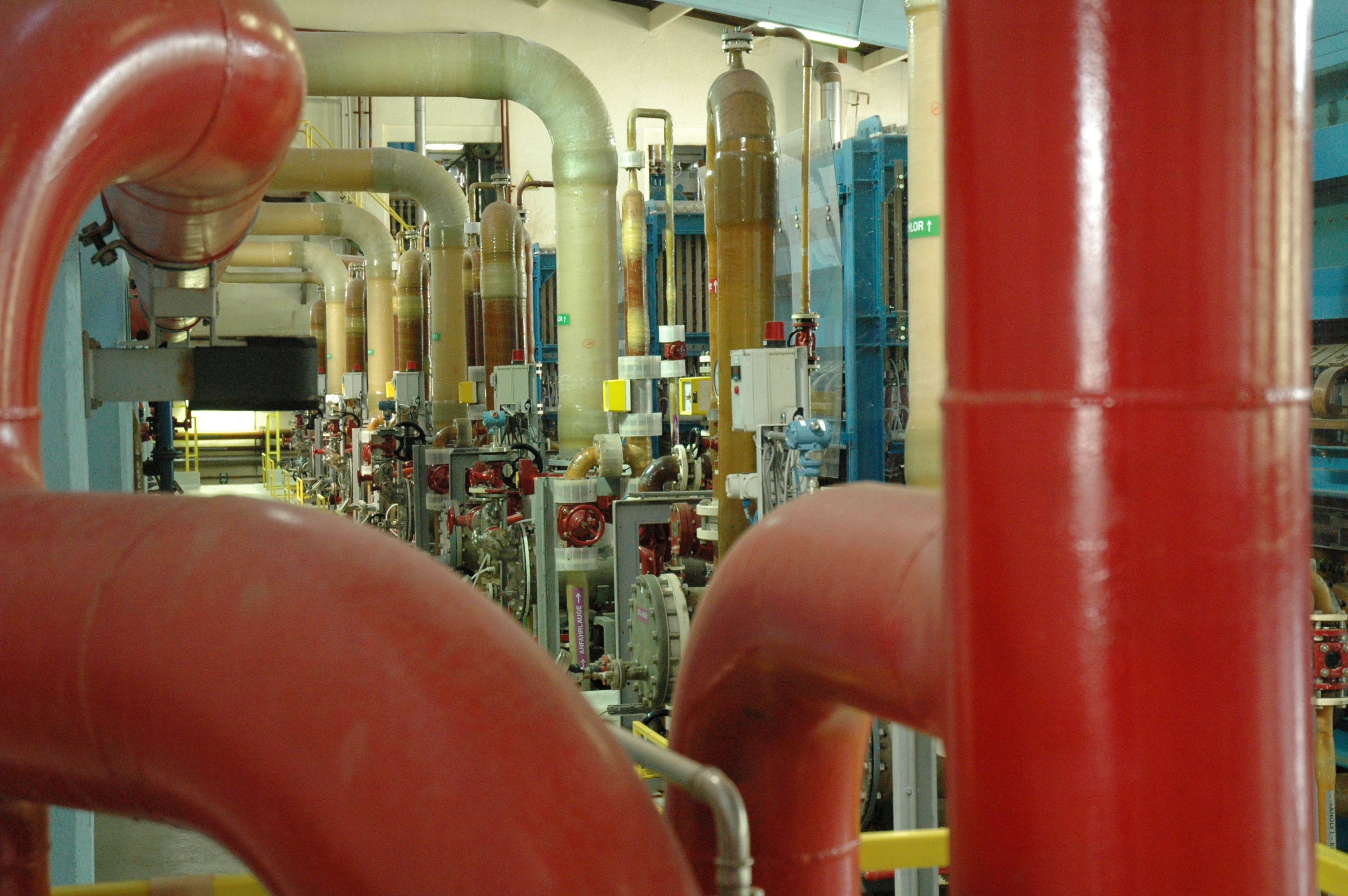 A complex industrial interior with large red and beige pipes, valves, and machinery, showcasing an intricate network in a factory or plant.