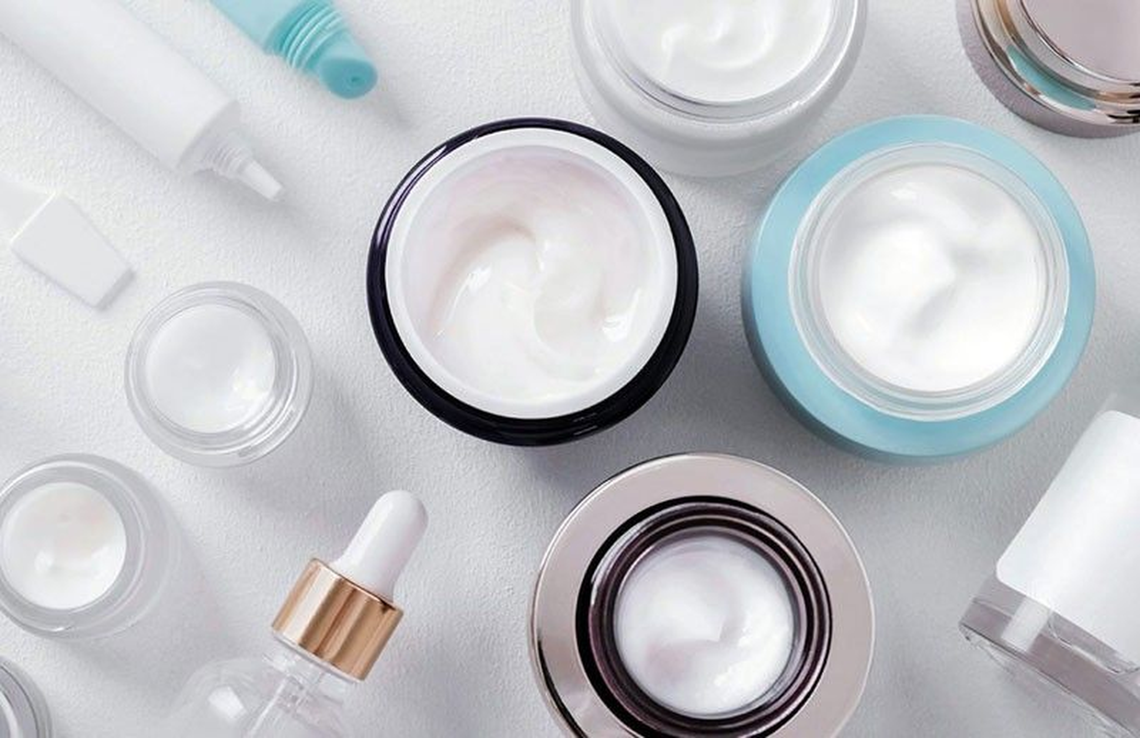 Assorted skincare containers, including jars and bottles with creams and serums, arranged on a white surface.