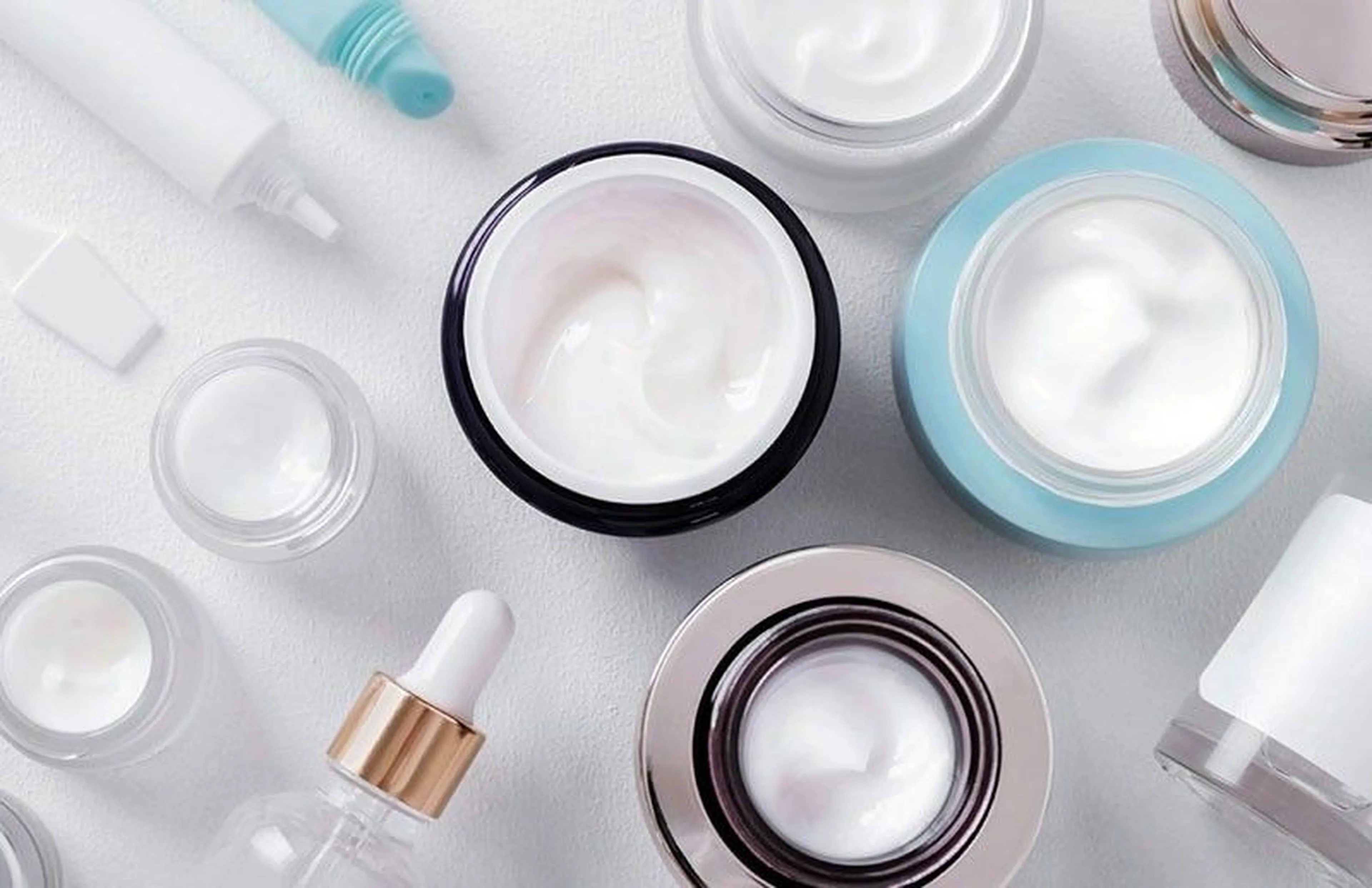 Assorted skincare containers, including jars and bottles with creams and serums, arranged on a white surface.
