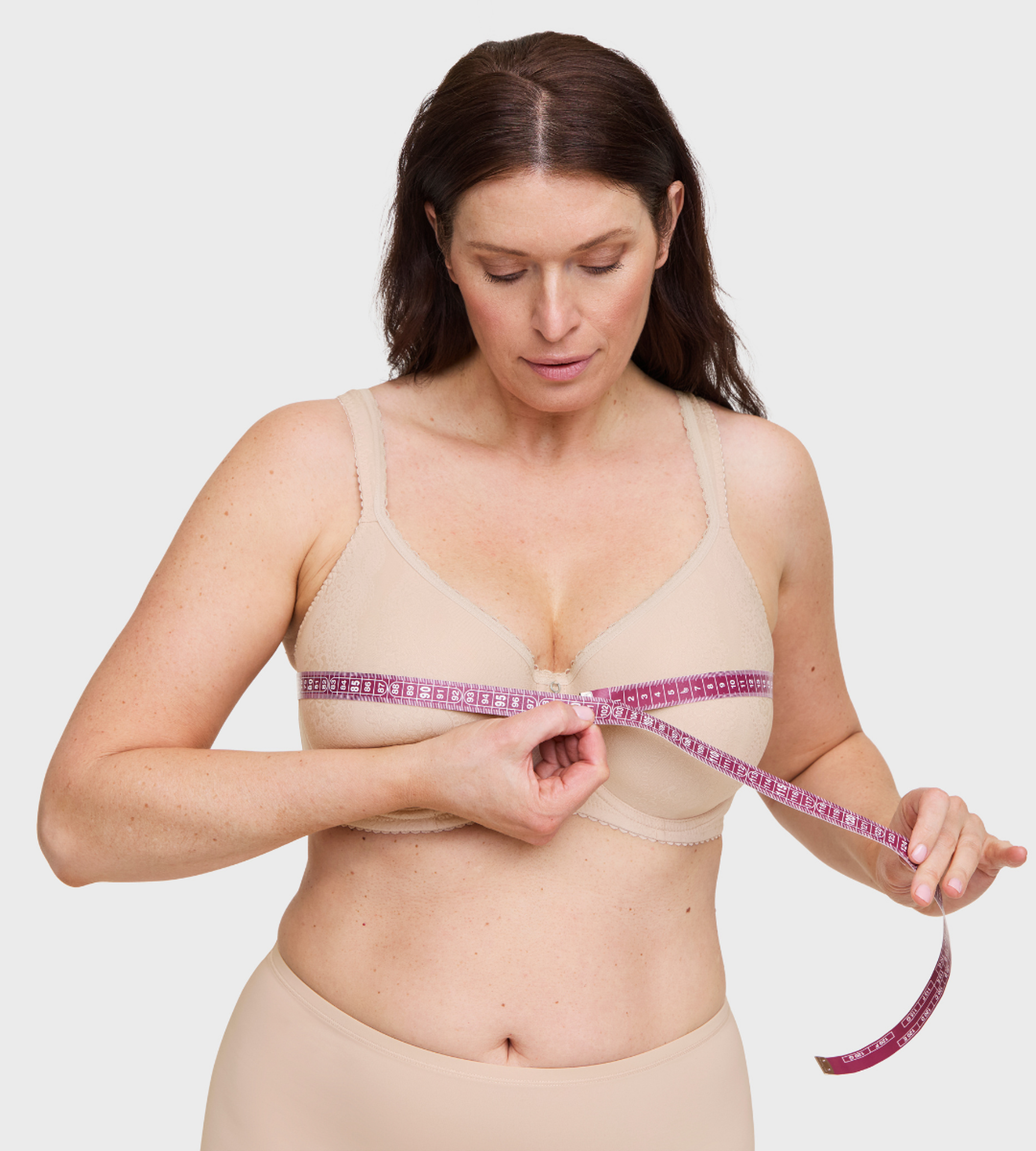 Woman in nude bra measuring her bust with a pink measuring tape to find correct bra size