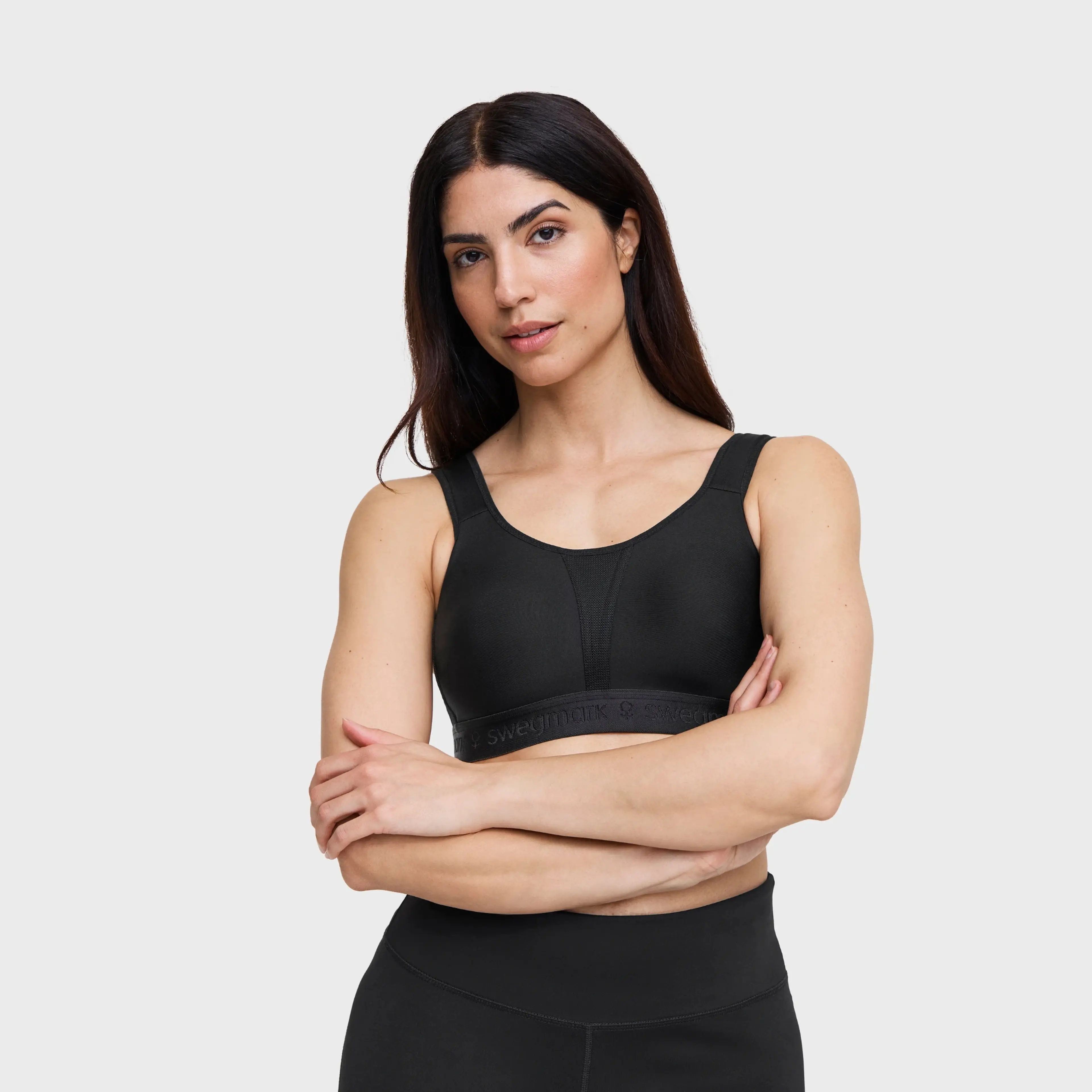 Woman with dark hair wearing a black Swegmark sports bra and leggings, arms crossed, against a light gray background.