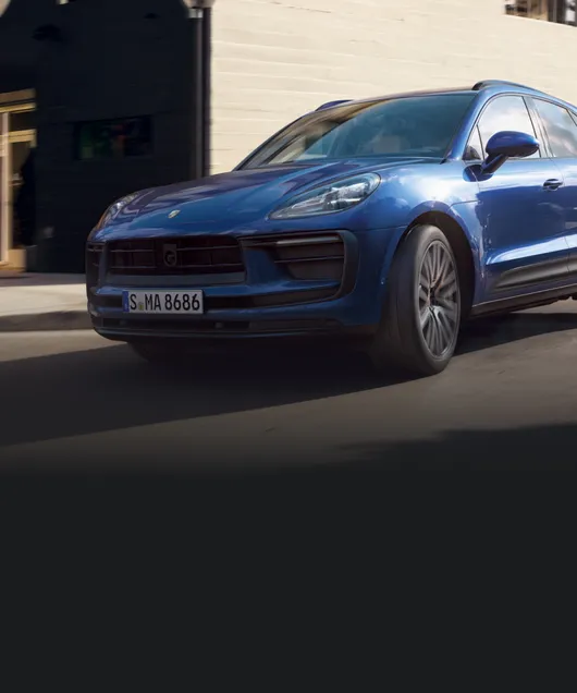 Un Porsche Macan en color Azul Gentian Metalizado circulando por la ciudad. Vista frontal y lateral.