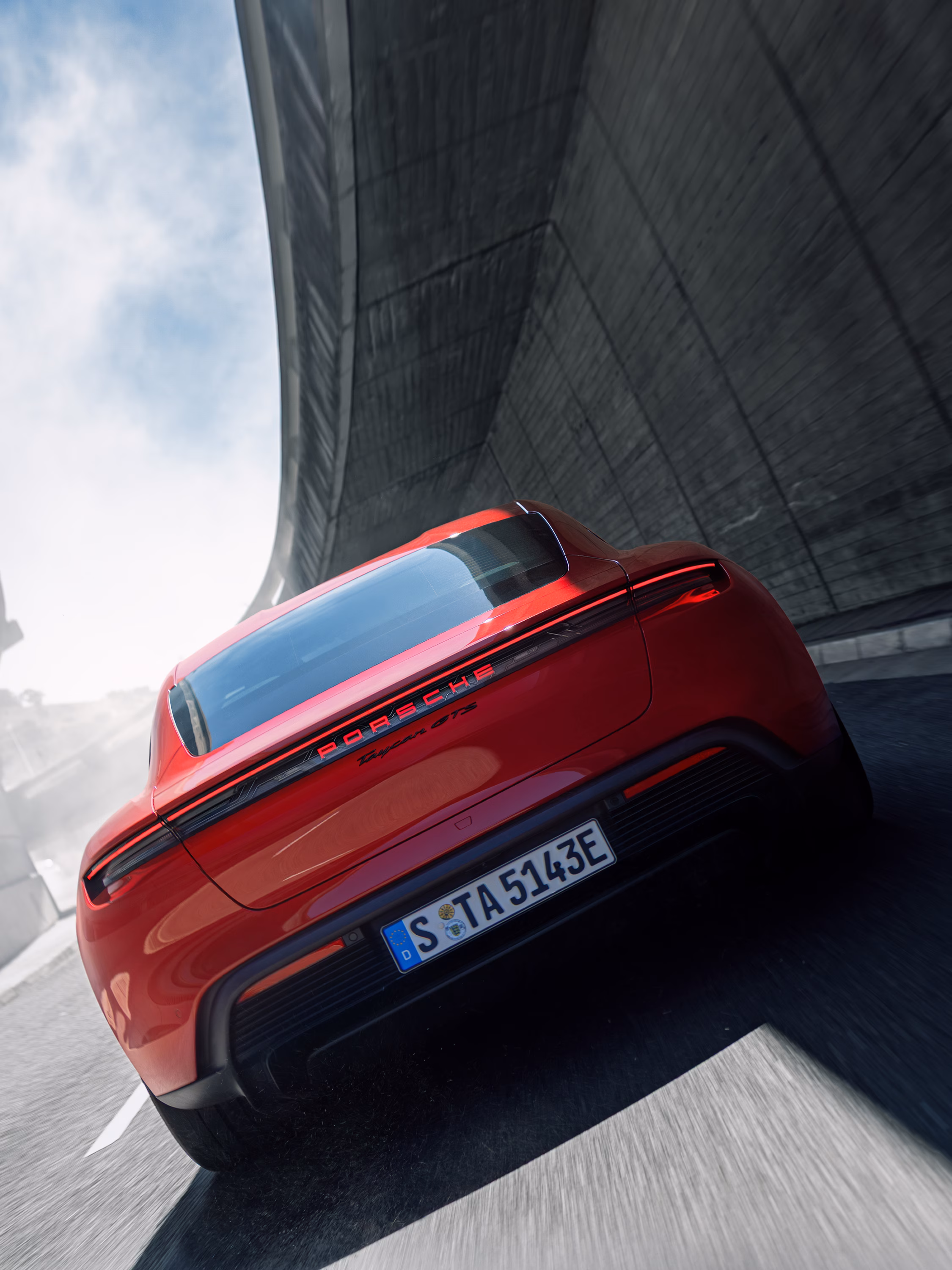 Side view of a moving Porsche Taycan GTS in Carmine Red.