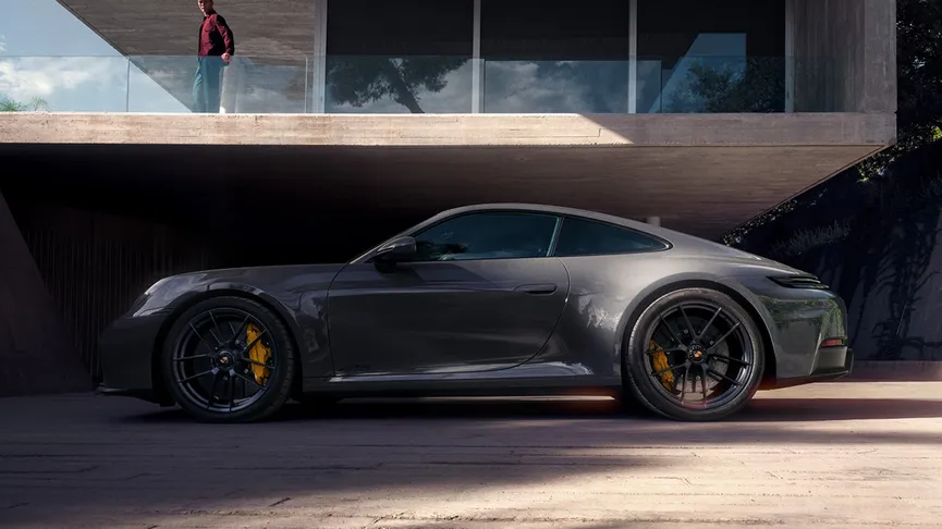 The new 911 Carrera GTS, in Vanadium Grey Metallic, parked outside a modern building, with someone looking down from the first-floor balcony.