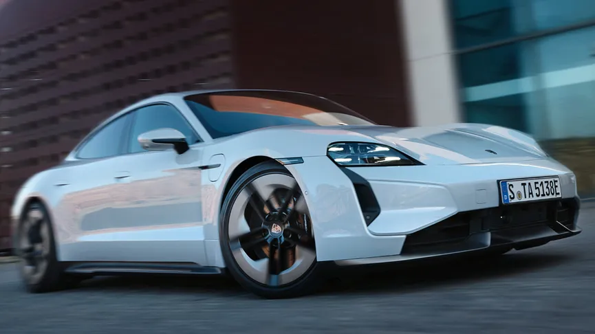 The Taycan Turbo S driving past a brown building.