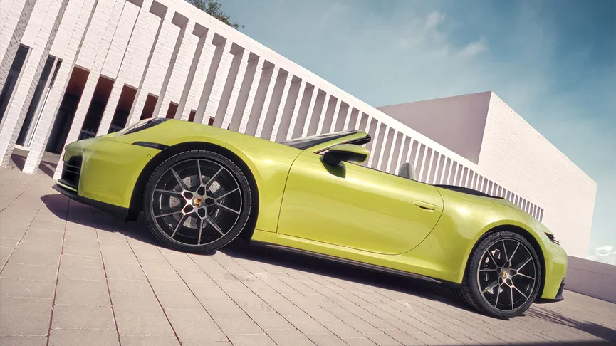 The new 911 Carrera Cabriolet, in Cartagena Yellow Metallic, parked outside a modern building, next to a white wall.