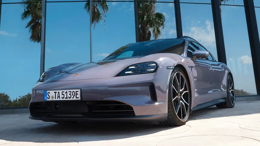 The Taycan 4S Sport Turismo in front of a glass building with palm trees reflecting off the glass.