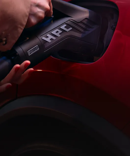 Nahaufnahme eines Ladesteckers mit der Aufschrift "HPC", der in die Ladebuchse eines Porsche Macan gesteckt wird.