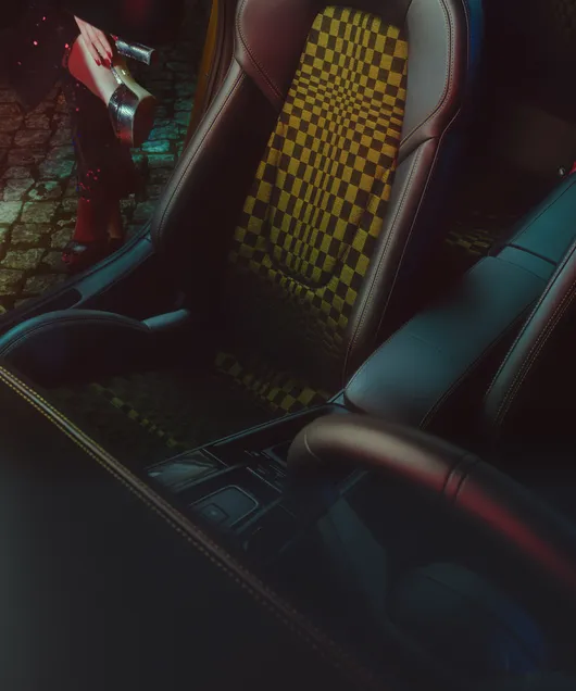 Widok fotela pasażera we wzór Pascha w Porsche 911 Spirit 70. W tle widać kobiece nogi w złotych butach na platformie.
