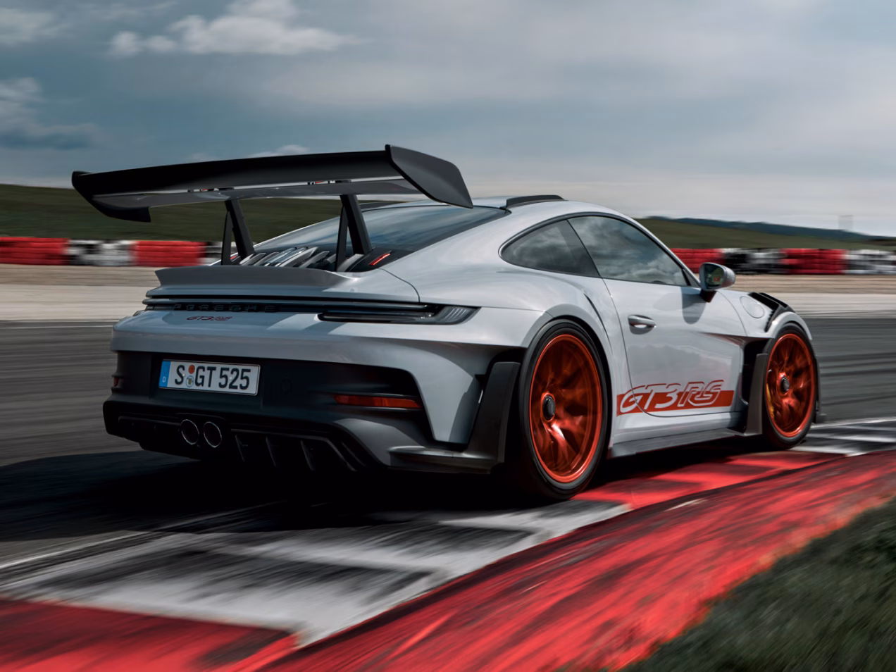 The Porsche 911 GT3 RS in Ice Grey Metallic taking a corner on a race track. Rear and side view from behind.