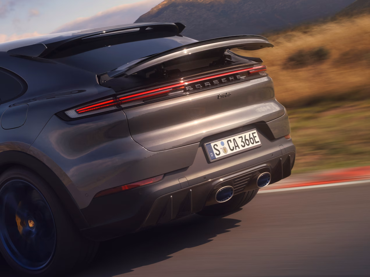 Porsche Cayenne Turbo E-Hybrid Coupé med GT-paket i Quarzite Grey Metallic. Detaljerad vy av baksidan med sportavgassystemet i titan.