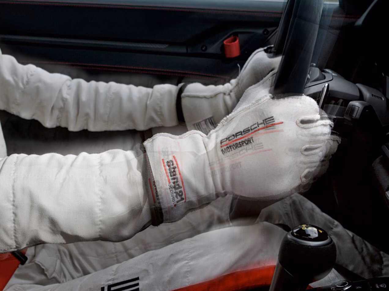 View into the cockpit of a Porsche 911 GT3 RS. A person wearing a racing suit and gloves is holding the steering wheel.