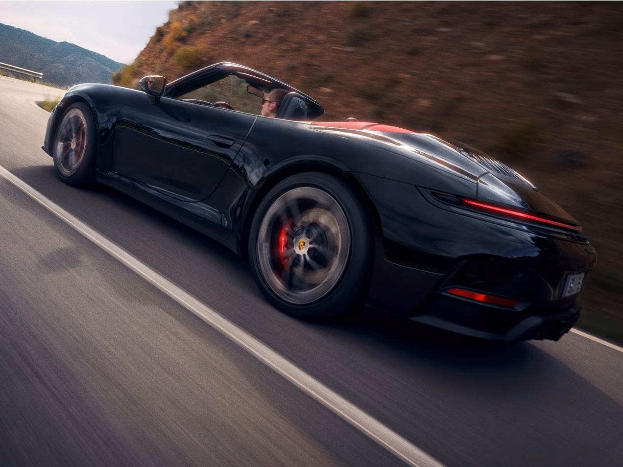 Porsche 911 Carrera GTS Cabriolet in Schwarz fährt auf Straße durch bergige Landschaft. Blick auf die Seite.